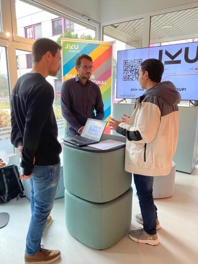 3 Menschen im Gespräch rund um einen Stehtisch. 