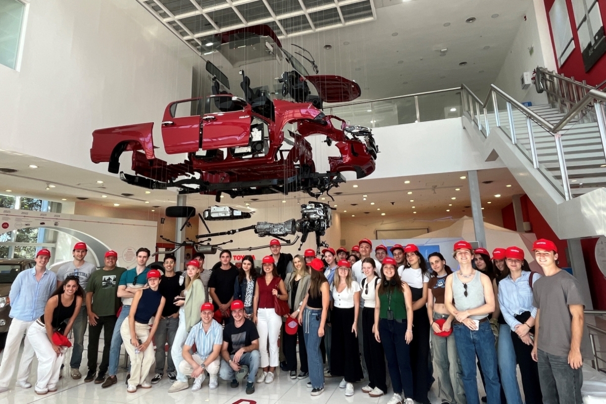 Gruppenfoto von Studierenden vor dem Modell eines Autos während eines Firmenbesuchs im Rahmen eines WU International Short Programs.