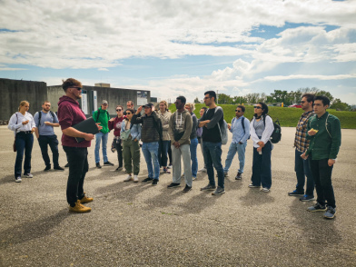 Gruppen von Studierenden die einem Guide zuhört // Groups of students listening to a guide